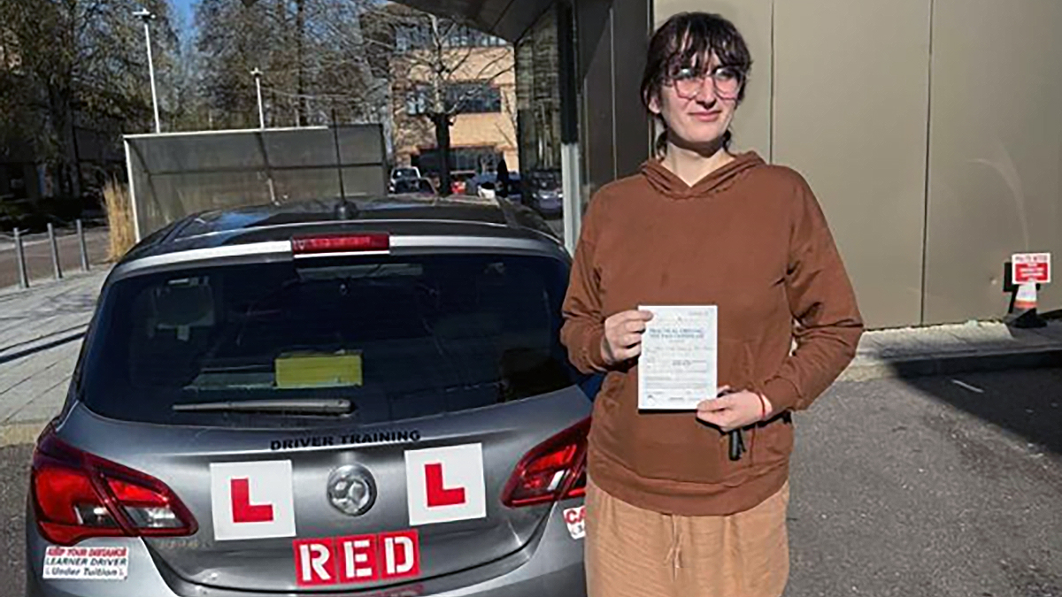 Imogen standing in front of a learner driver car holding her driving test pass certificate